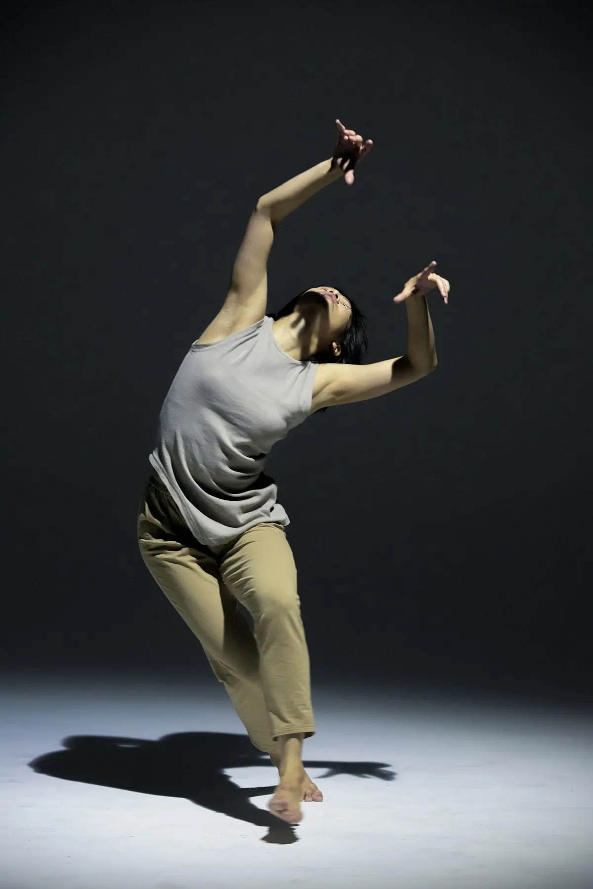 A dancer suspended mid-fall in the dark, weight already committed to the floor.