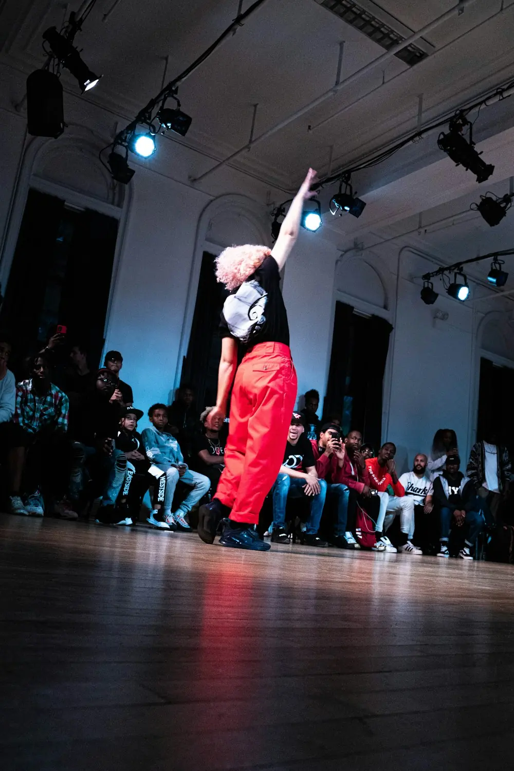 A soloist under a single light with the audience standing along the wall.