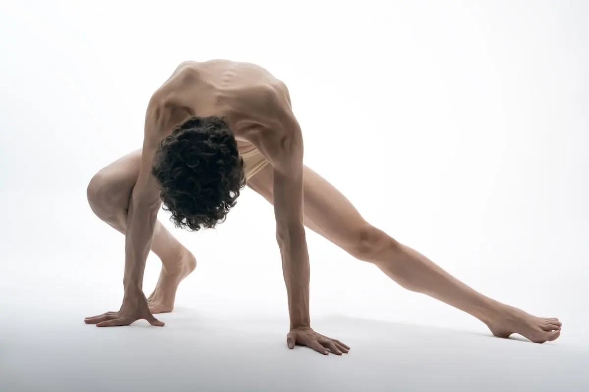 A dancer on all fours transitioning through a low position against a pale wall.