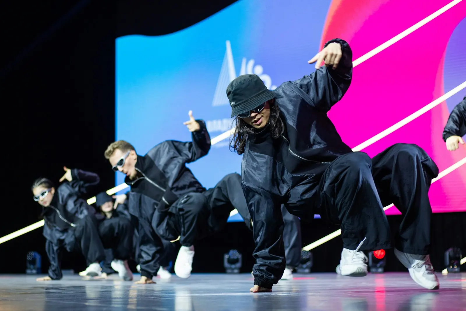 A group finishing a routine on stage under blue and pink light.